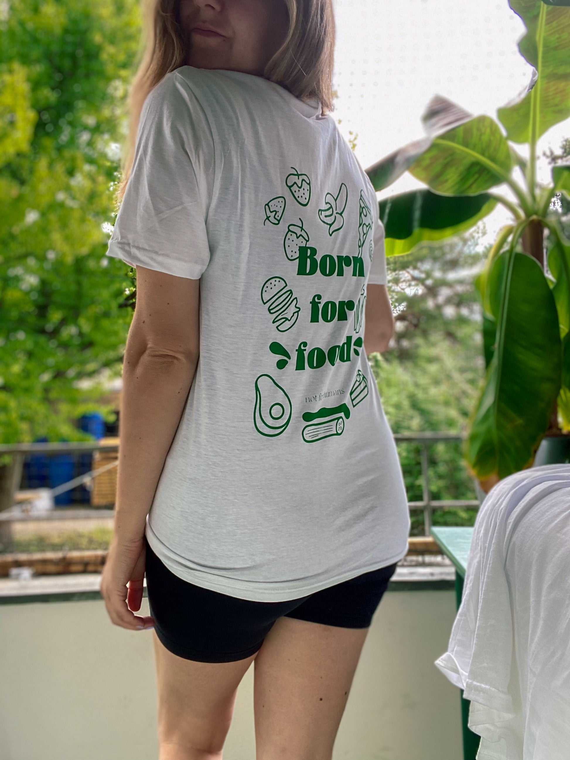 Weißes T-Shirt mit der Aufschrift "Born for food – not for humans" auf dem Rücken. Umrandet von diversen Lebensmitteln